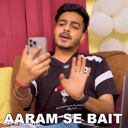 Man Sitting On Couch Looking At Phone Says Aaram-Se-Bait GIF