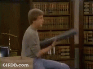 Man Sitting On Desk Holding Sword Surrounded By People GIF