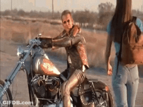 Man Sitting On Motorcycle In Desert, Woman Behind GIF