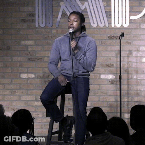 Man Sitting On Stool Speaking Into Microphone In Front Of Brick Wall GIF