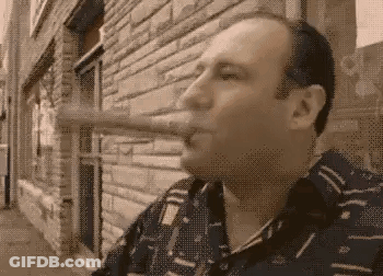 Man Smoking Cigar Outside Brick Building GIF