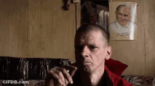 Man Smoking Cigarette In Front Of Picture Named John GIF