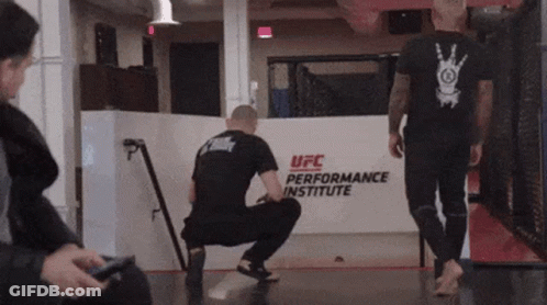 Man Squatting In Front Of UFC Performance Institute Sign GIF