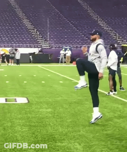 Man Squatting On Football Field In Front Of Stadium GIF