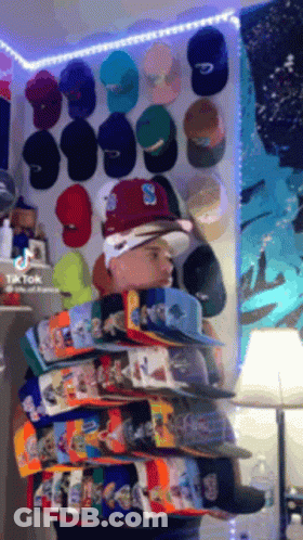 Man Standing Before Wall Of Hats With Letter S GIF