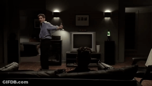 Man Standing Beside Man Sitting On Couch Watching TV GIF