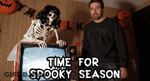Man Standing Beside Skeleton In Front Of TV Saying Time For Spooky Season GIF