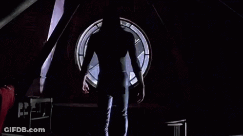 Man Standing In Dark Room Before Round Window GIF