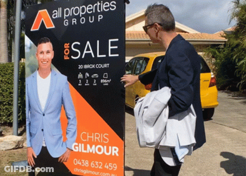 Man Standing In Front Of All Properties Group Sign GIF