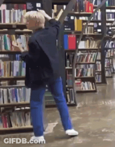 Man Standing In Front Of Bookshelf In Bookstore GIF
