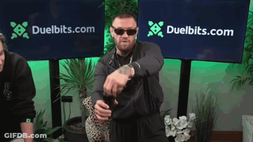 Man Standing In Front Of Duelbits Banner GIF