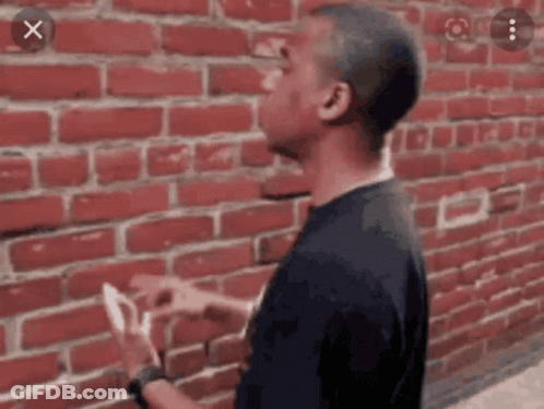 Man Standing In Front Of Red Brick Wall Holding Paper GIF