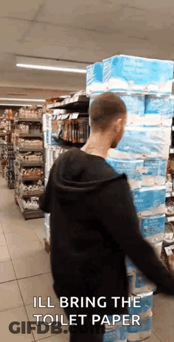 Man Standing In Front Of Stacked Toilet Paper Rolls GIF
