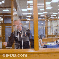 Man Standing In Front Of Window With Woman At Desk GIF