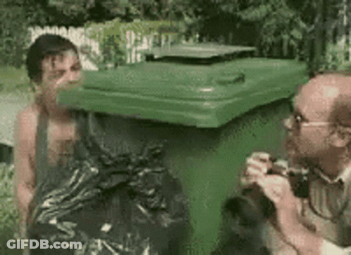 Man Standing Next To Green Trash Can While Another Takes Picture GIF