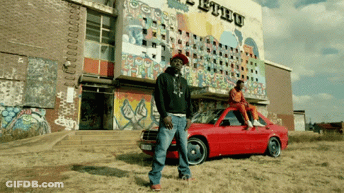 Man Standing Next To Red Car In Front Of Ethu Building GIF