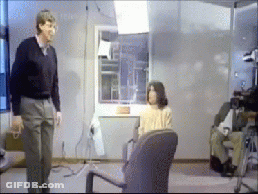 Man Standing Next To Woman In Chair GIF