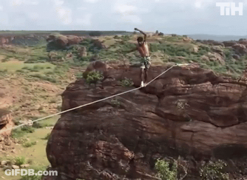 Man Standing On Rope On Rocky Cliff With Letters TH GIF