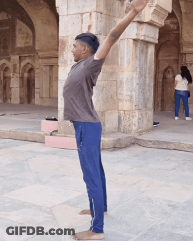 Man Stretching Arms In Front Of Stone Building GIF