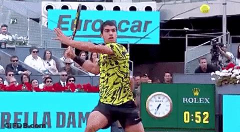 Man Swinging Tennis Racket At Ball In Front Of Rolex Sign GIF