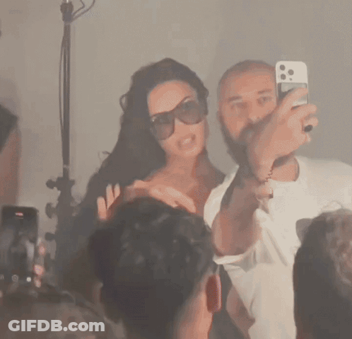 Man Taking Picture Of Woman In Sunglasses In Front Of Crowd GIF