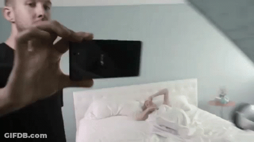 Man Taking Picture Of Woman Laying On Bed GIF
