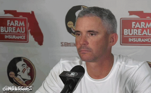 Man Talking Into Microphone In Front Of Farm Bureau Sign GIF