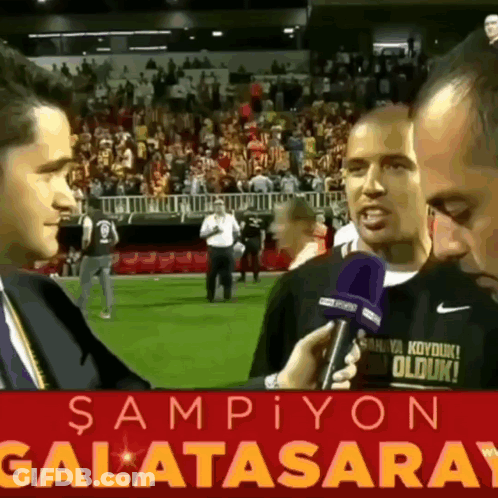 Man Talking Into Microphone In Front Of Galatasaray Sign GIF