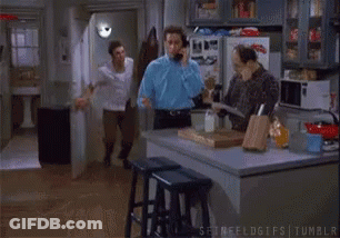 Man Talking On Phone While Another Man Dances In Kitchen GIF