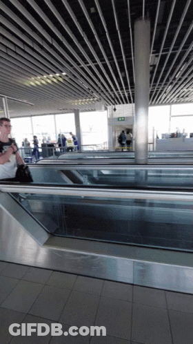 Man Walking Down Escalator With Exit Sign GIF