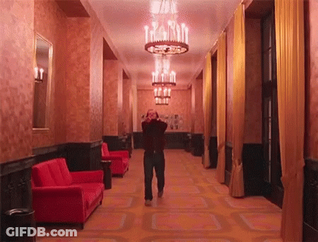 Man Walking Down Hallway With Chandelier And Red Couch GIF