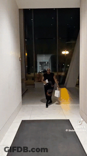 Man Walking Down Hallway With Shopping Bag And Purse GIF