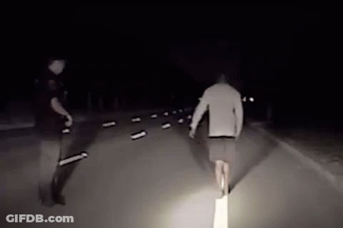 Man Walking Down Road At Night With Police Officer Behind GIF