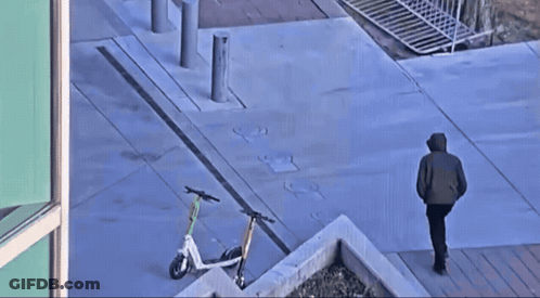 Man Walking Down Sidewalk With Parked Scooters GIF