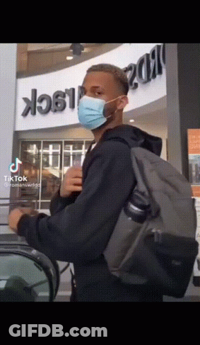 Man Wearing Mask And Backpack In Front Of Romans Wildp Sign GIF