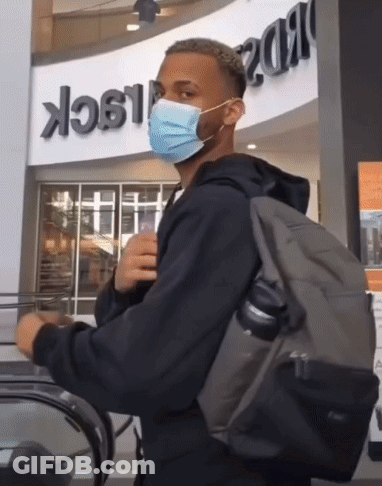 Man Wearing Mask And Backpack Riding Escalator GIF