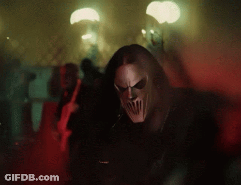 Man Wearing Mask Standing In Dark Room With People Behind GIF