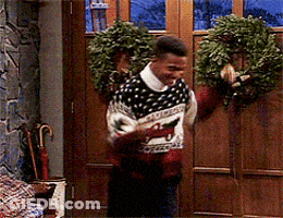 Man Wearing Sweater With Horse Stands In Front Of Door With Wreath GIF