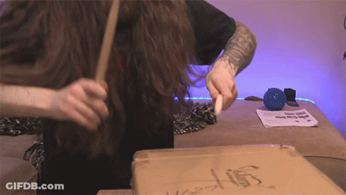 Man With Arm Tattoo Holding Stick In Front Of Cardboard Box Saying Stump GIF