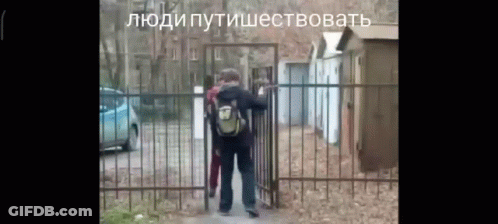 Man With Backpack In Front Of Fence With Russian Writing GIF