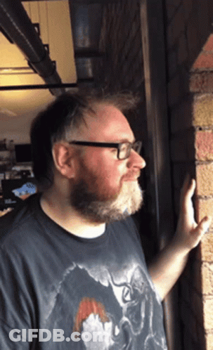 Man With Beard And Glasses Leaning Against Wall GIF