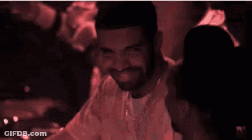 Man With Beard And Necklace Smiles In Dark Room GIF