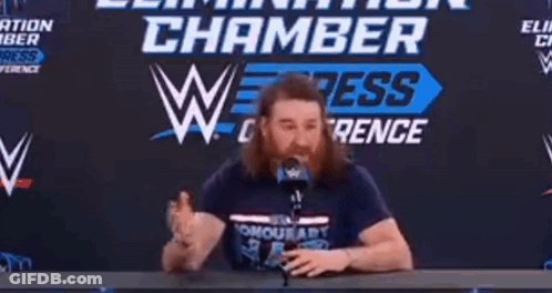 Man With Beard At Table With Microphone Chamber Sign GIF