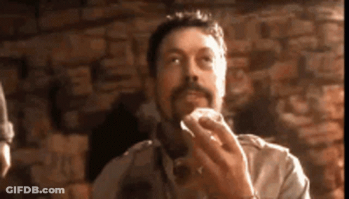 Man With Beard Eating Hamburger In Front Of Brick Wall GIF