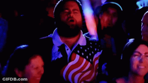 Man With Beard In American Flag Shirt Sitting In Crowd GIF