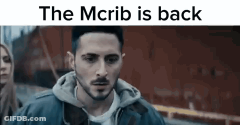 Man With Beard In Front Of Red Building Saying The McRib Is Back GIF