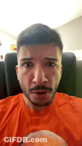 Man With Beard In Orange Shirt Looking At Camera GIF