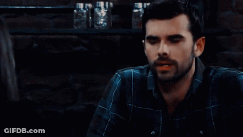 Man With Beard In Plaid Shirt Sitting In Dark Room GIF