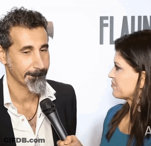 Man With Beard Interviewed By Woman In Front Of Flaunt Wall GIF