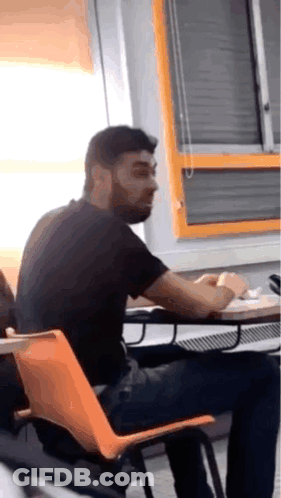 Man With Beard Sitting At Table In Classroom GIF